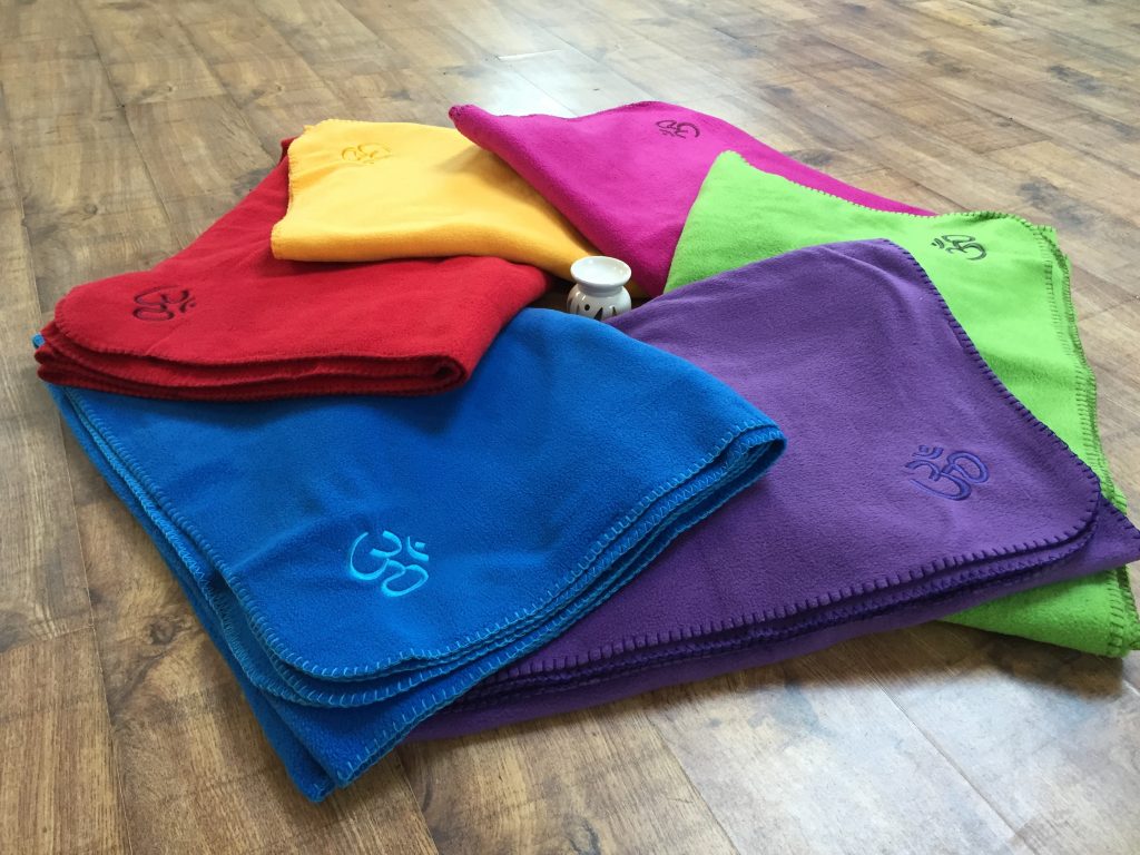 Folded yoga blankets in her class colours on a hall floor